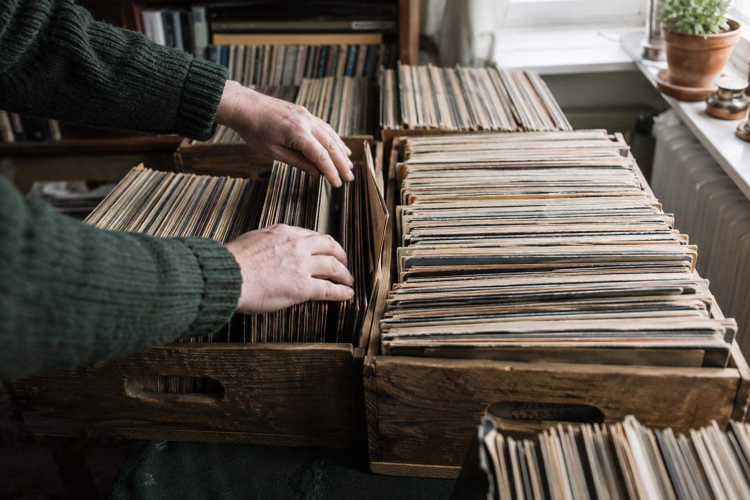 Händer som varsamt bläddrar bland vinylskivor i träbackar